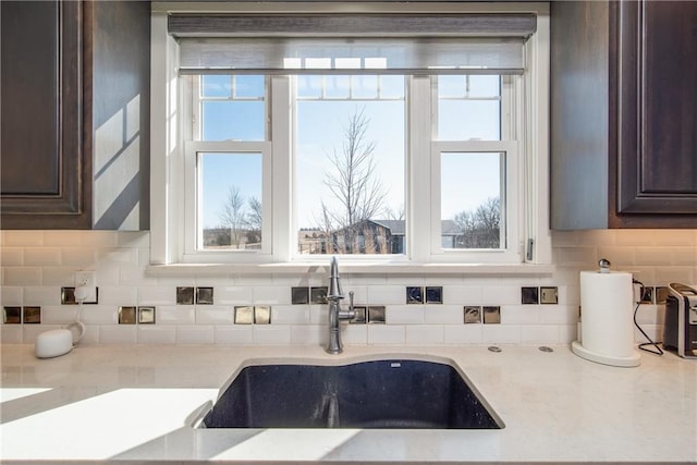 kitchen featuring a sink, backsplash, dark brown cabinets, and a healthy amount of sunlight