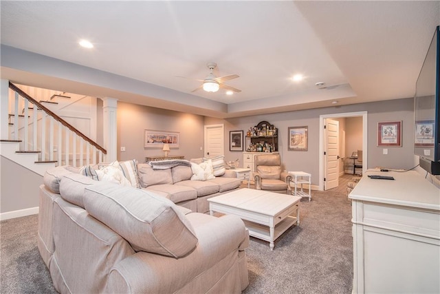 living room featuring baseboards, light colored carpet, stairs, a raised ceiling, and a ceiling fan