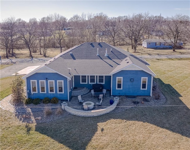 rear view of house with a shingled roof, a patio, a lawn, and a fire pit