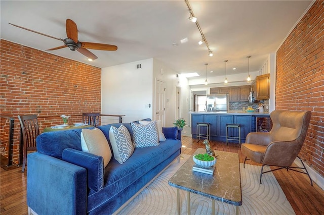 living area featuring visible vents, brick wall, rail lighting, wood finished floors, and a ceiling fan