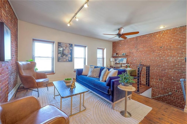 living area featuring brick wall, a fireplace, a ceiling fan, and wood-type flooring