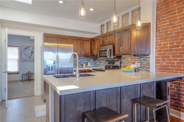 kitchen featuring a peninsula, a sink, decorative backsplash, stainless steel appliances, and pendant lighting