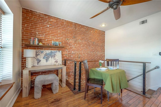 dining area with visible vents, baseboards, brick wall, and hardwood / wood-style flooring