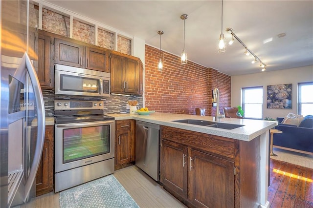 kitchen with a sink, open floor plan, appliances with stainless steel finishes, a peninsula, and light countertops