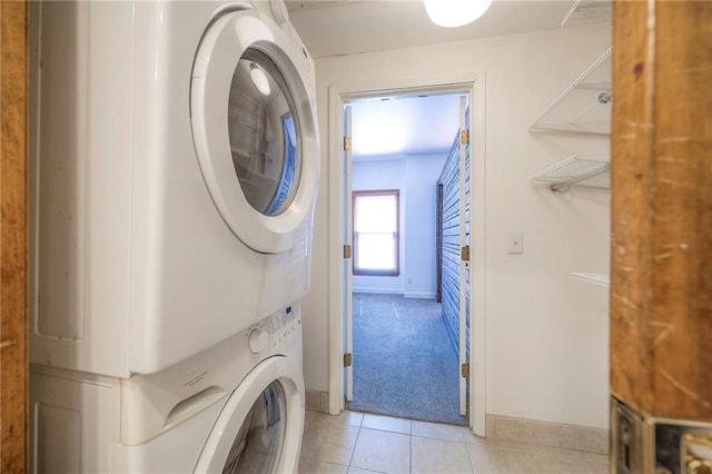 clothes washing area with stacked washer / dryer, baseboards, light colored carpet, light tile patterned floors, and laundry area