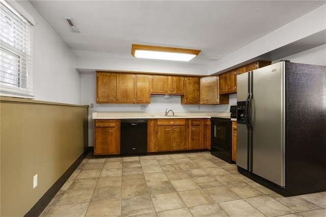 kitchen featuring visible vents, black appliances, a sink, brown cabinetry, and light countertops