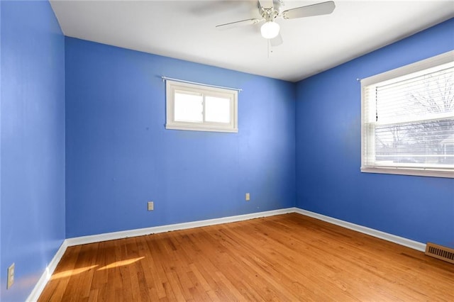 empty room featuring ceiling fan, visible vents, baseboards, and wood finished floors