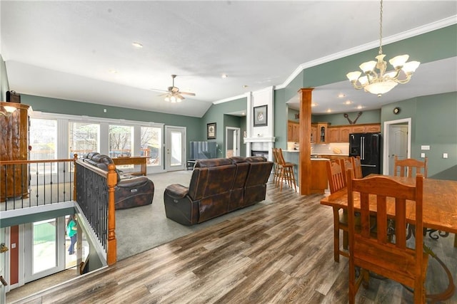 living area with crown molding, vaulted ceiling, ceiling fan with notable chandelier, a fireplace, and wood finished floors