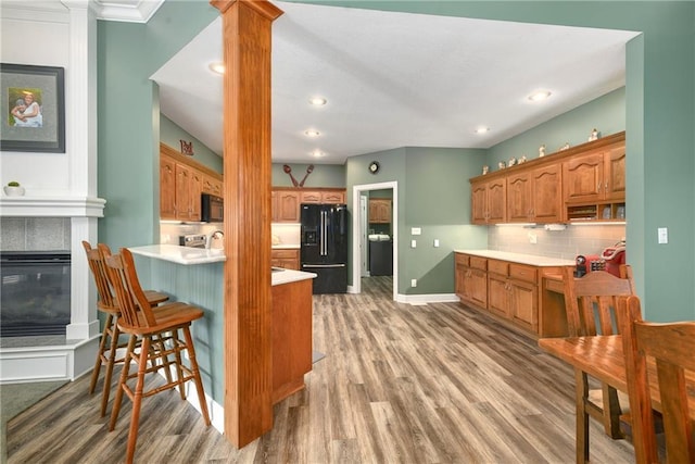 kitchen with light wood finished floors, a peninsula, black appliances, light countertops, and brown cabinets