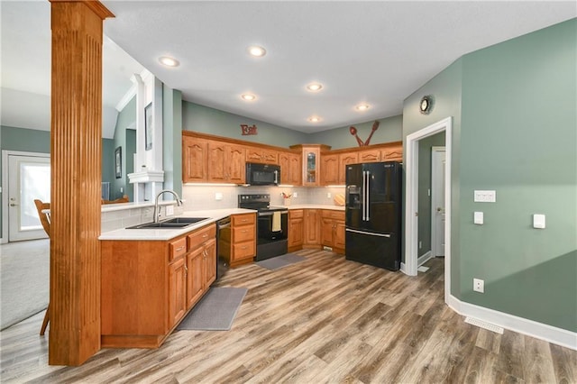 kitchen with tasteful backsplash, glass insert cabinets, decorative columns, black appliances, and a sink