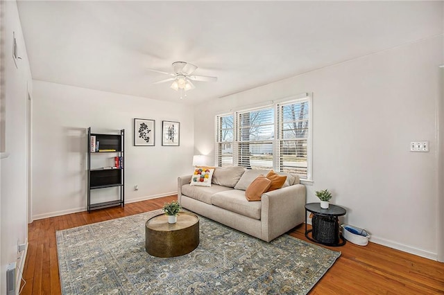 living area featuring baseboards, a ceiling fan, and wood-type flooring