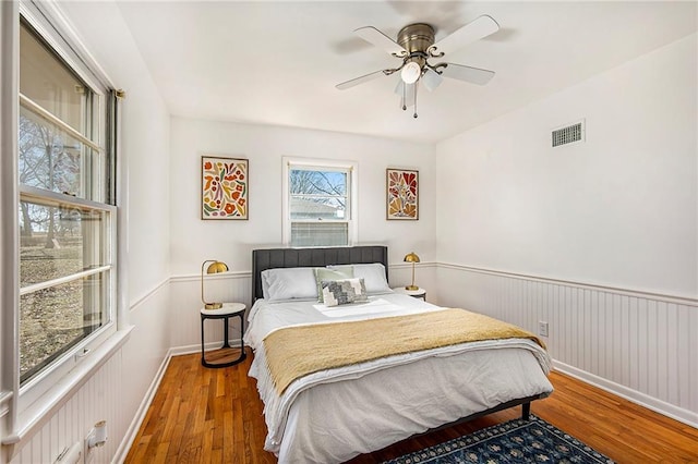 bedroom featuring visible vents, wainscoting, a ceiling fan, and hardwood / wood-style floors