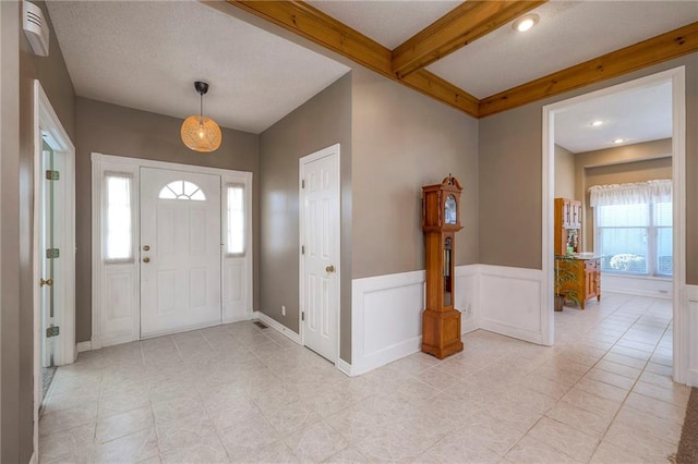 foyer with beamed ceiling, wainscoting, and a decorative wall