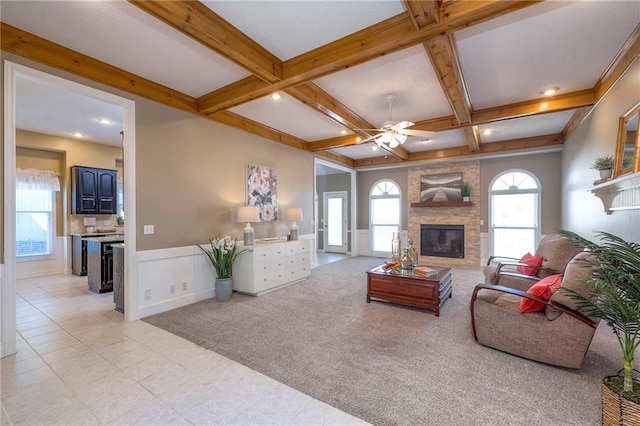 living area with beamed ceiling, a large fireplace, plenty of natural light, and a wainscoted wall