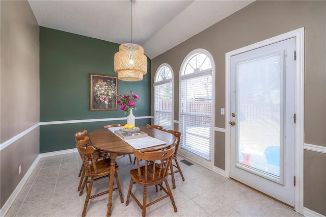 dining room with light tile patterned floors, visible vents, lofted ceiling, and baseboards