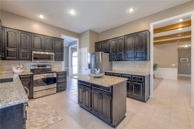 kitchen featuring backsplash, a kitchen island, stainless steel appliances, light tile patterned flooring, and light stone countertops