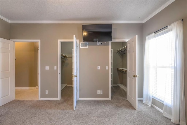 unfurnished bedroom featuring a walk in closet, carpet floors, a textured ceiling, and crown molding