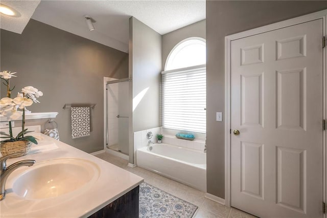 full bathroom featuring a garden tub, a stall shower, a sink, a textured ceiling, and tile patterned flooring