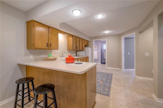 kitchen featuring white microwave, a peninsula, light countertops, a textured ceiling, and a kitchen bar