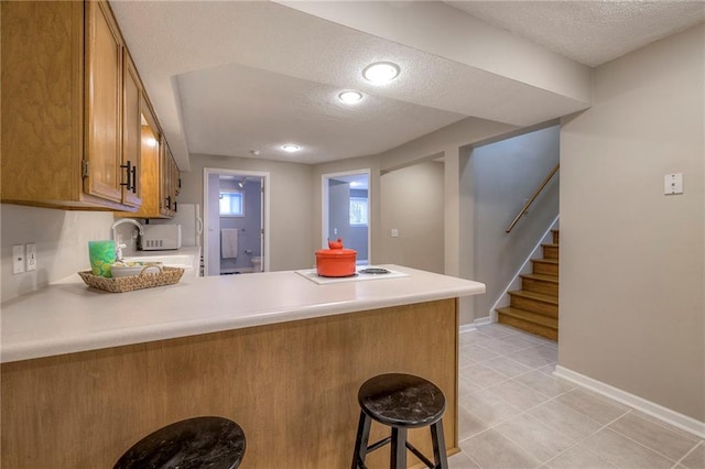 kitchen featuring brown cabinets, a peninsula, a textured ceiling, and light countertops