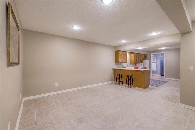 kitchen with brown cabinetry, a peninsula, light countertops, and baseboards