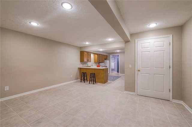 kitchen featuring a peninsula, light countertops, brown cabinets, and baseboards