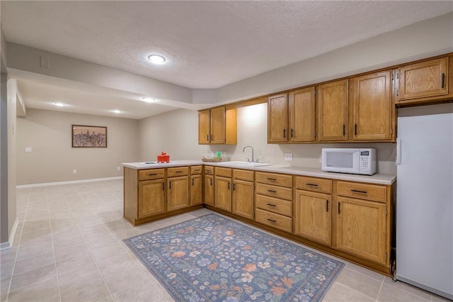 kitchen featuring brown cabinets, white appliances, a peninsula, and a sink