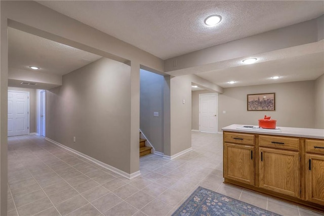 kitchen with a textured ceiling, light tile patterned flooring, brown cabinetry, light countertops, and baseboards