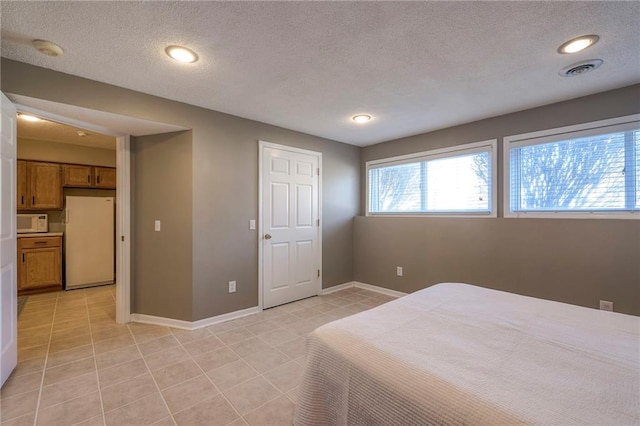 bedroom featuring visible vents, baseboards, light tile patterned floors, freestanding refrigerator, and a textured ceiling