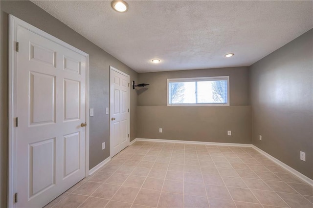 interior space featuring light tile patterned floors, a textured ceiling, and baseboards