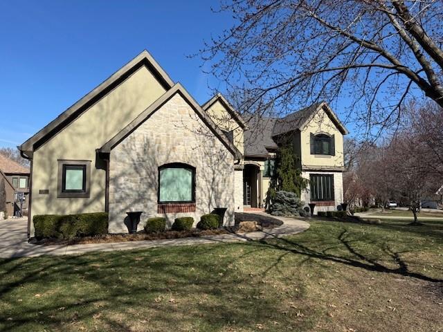 french country style house with stone siding, stucco siding, and a front lawn