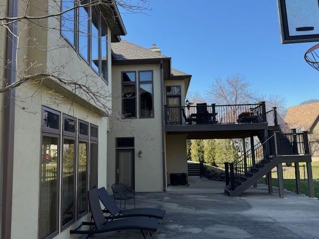 back of house with stairway, a wooden deck, stucco siding, and a patio area