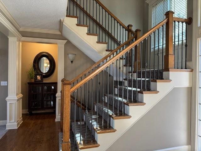 staircase featuring crown molding, wood finished floors, baseboards, and ornate columns