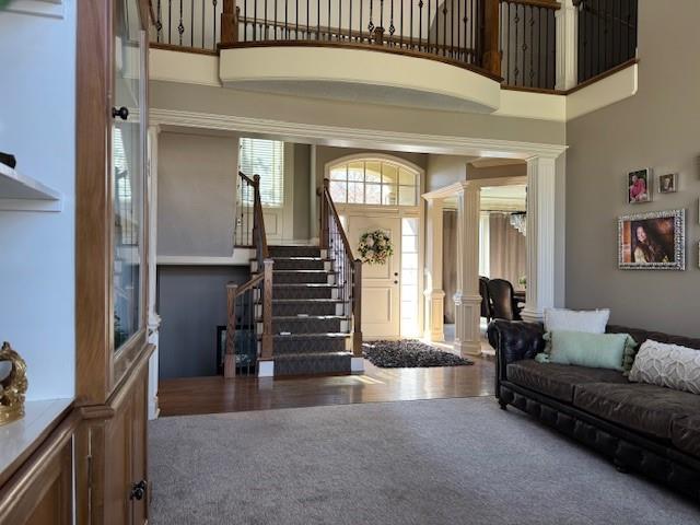 interior space featuring stairs, a towering ceiling, wood finished floors, and ornate columns