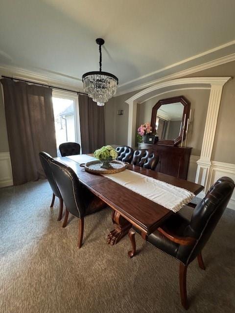 carpeted dining area with a notable chandelier, a decorative wall, wainscoting, and ornamental molding