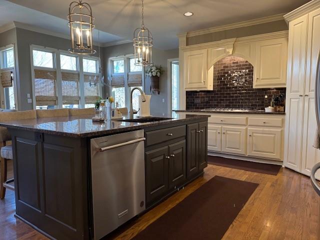 kitchen with dark wood-style floors, a center island with sink, ornamental molding, a sink, and stainless steel dishwasher