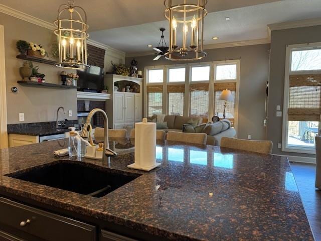 kitchen featuring crown molding, dark stone counters, a fireplace, and a sink