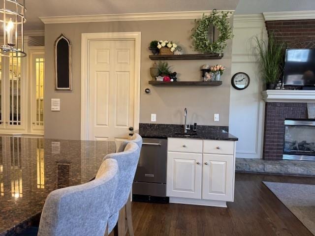 kitchen featuring dishwasher, ornamental molding, dark stone countertops, white cabinetry, and a sink