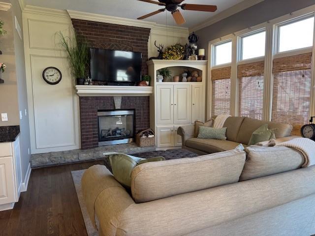 living room featuring crown molding, a brick fireplace, a ceiling fan, and dark wood-style flooring