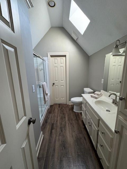 bathroom with a shower stall, toilet, vaulted ceiling with skylight, wood finished floors, and vanity