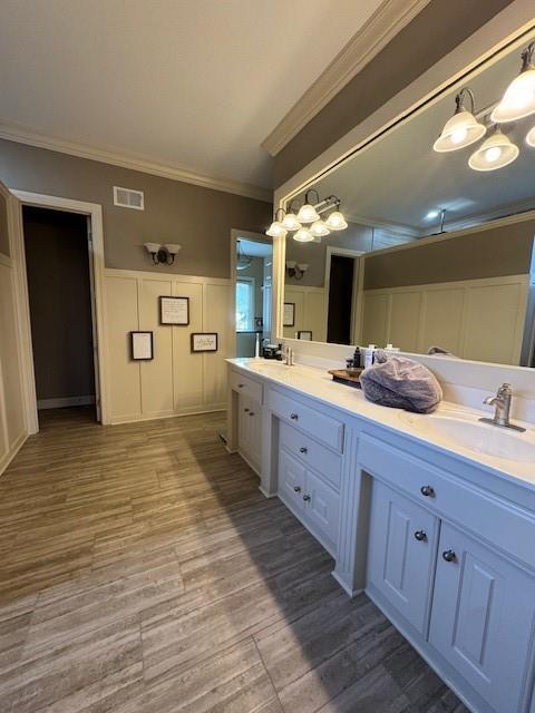 full bathroom featuring visible vents, a sink, wood finished floors, crown molding, and double vanity