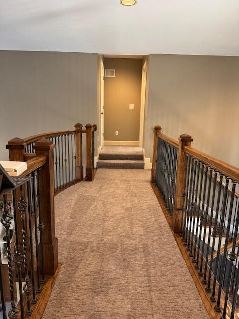 corridor with an upstairs landing, visible vents, baseboards, and carpet floors