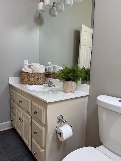 half bathroom with baseboards, toilet, and vanity