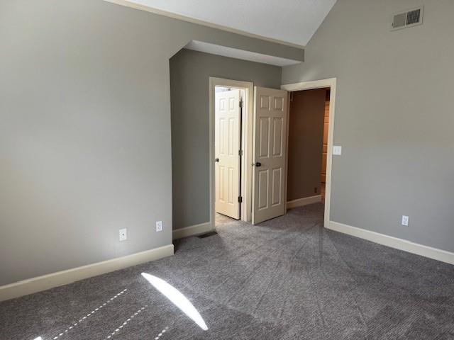 unfurnished room featuring lofted ceiling, carpet, baseboards, and visible vents