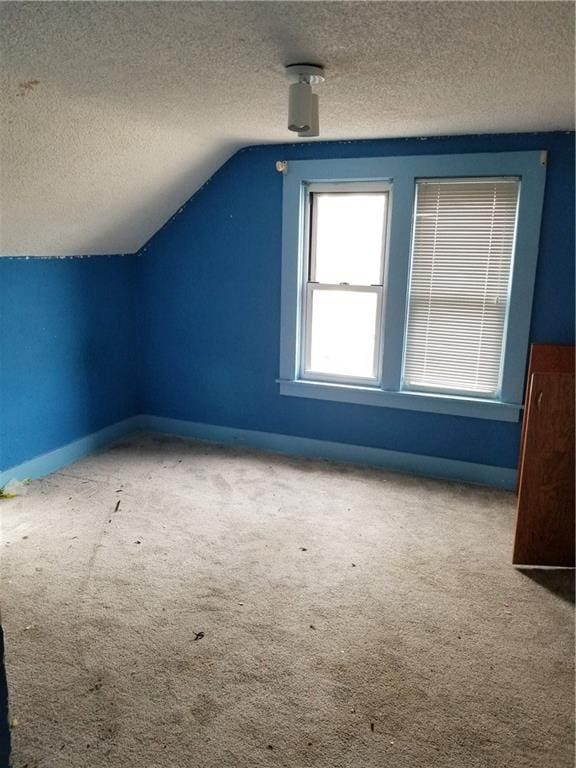 bonus room featuring lofted ceiling, carpet, baseboards, and a textured ceiling