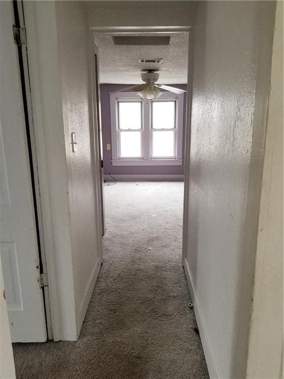 hall featuring visible vents, baseboards, carpet, a textured wall, and a textured ceiling