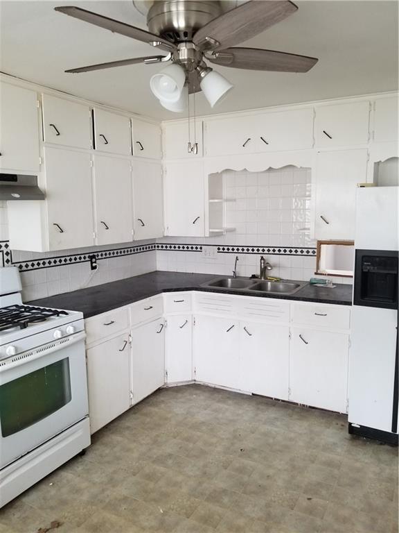 kitchen featuring under cabinet range hood, white appliances, dark countertops, and a sink