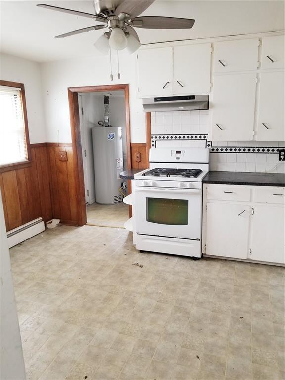 kitchen with under cabinet range hood, a wainscoted wall, white gas range oven, water heater, and a baseboard radiator