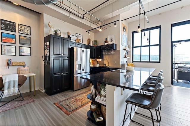 kitchen with a breakfast bar, a sink, decorative backsplash, stainless steel fridge, and light wood-type flooring