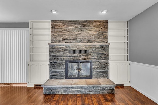 unfurnished living room with dark wood finished floors, built in shelves, a fireplace with raised hearth, and visible vents